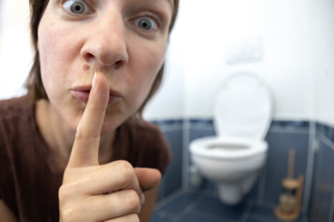Frau die vor einem WC Zeigefinger an die Lippen hält