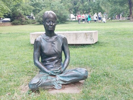 Baumkreis im Stadtpark in Graz, Statue im Schneidersitz im Gras