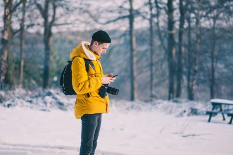 Mann steht mit Handy im Schnee